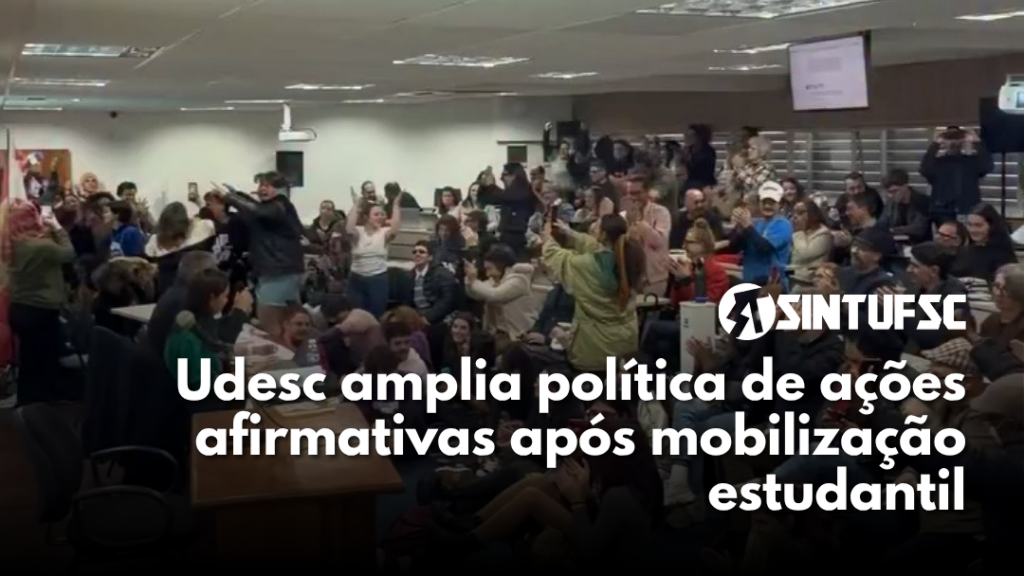 grupo de pessoas em pé, comemorando, em uma sala lotada. Com o texto "Udesc amplia política de ações afirmativas após mobilização estudantil"