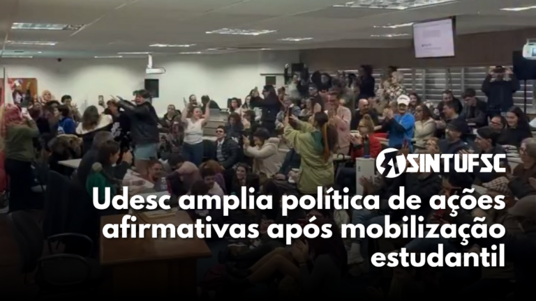 grupo de pessoas em pé, comemorando, em uma sala lotada. Com o texto "Udesc amplia política de ações afirmativas após mobilização estudantil"